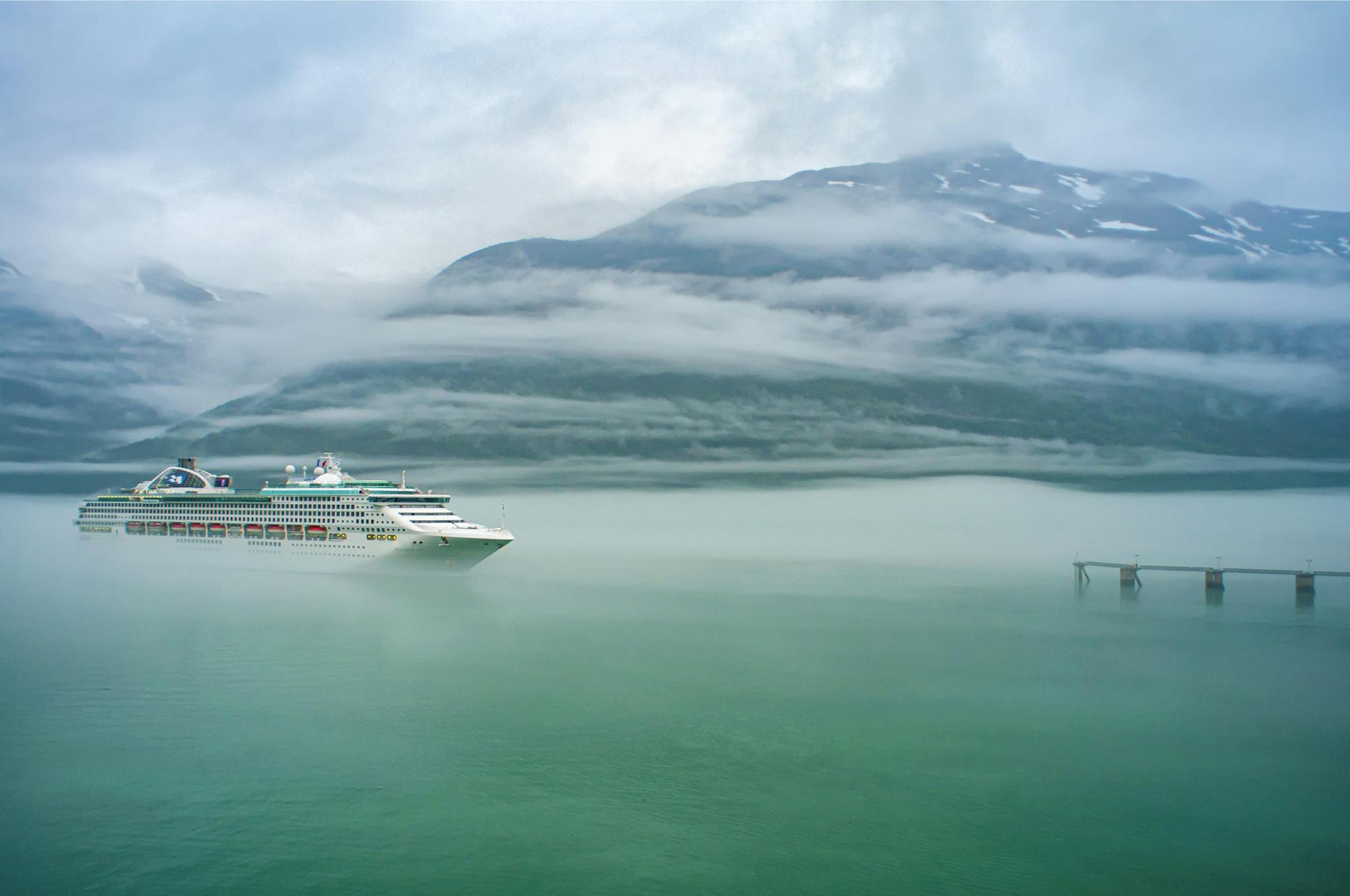 Cruise ship sailing through a misty fjord beneath snow-capped mountains