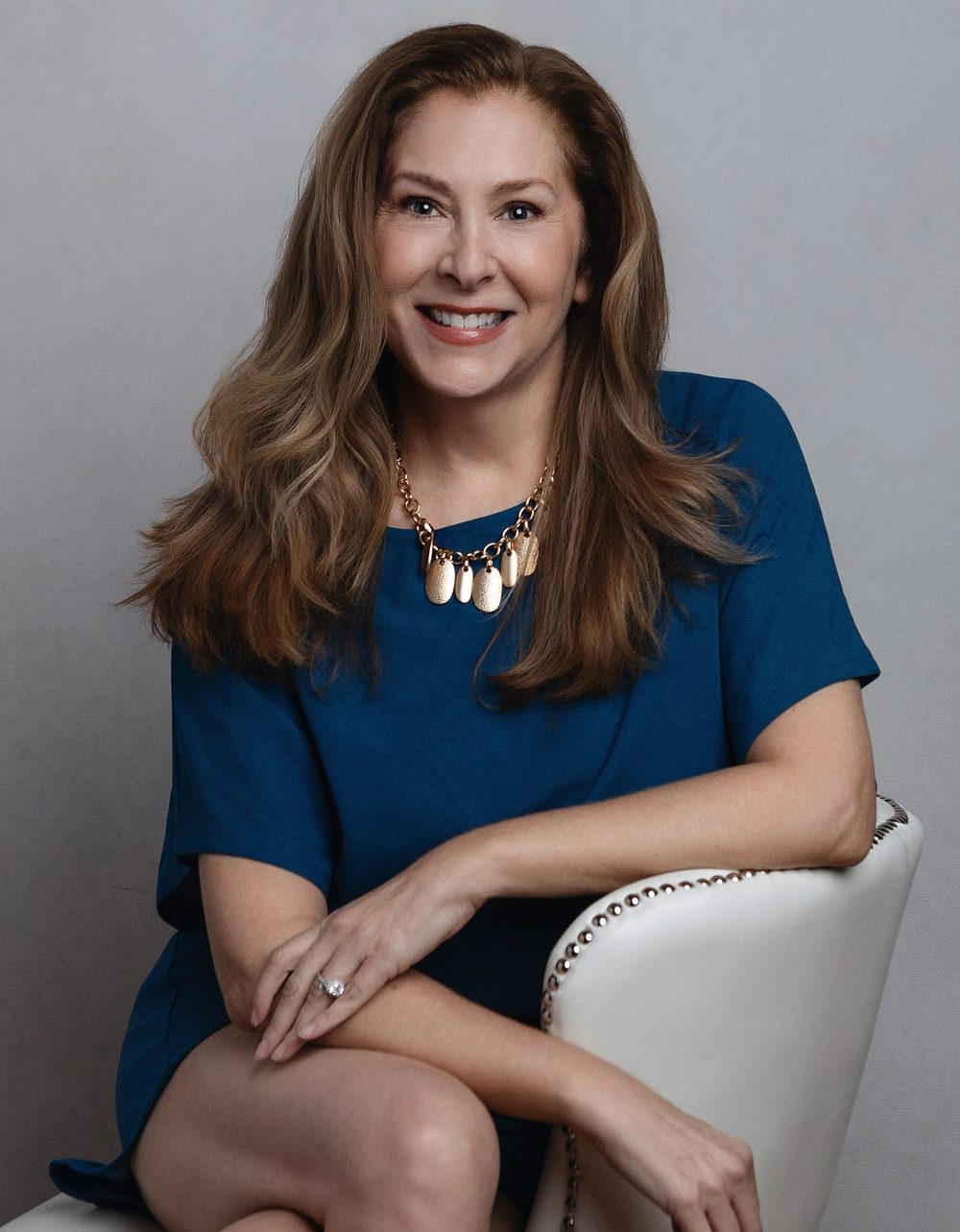 Vanessa Allen in a blue dress, seated in a white chair